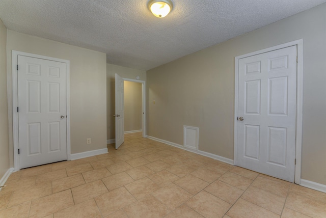 unfurnished bedroom with light tile patterned flooring, a textured ceiling, and baseboards