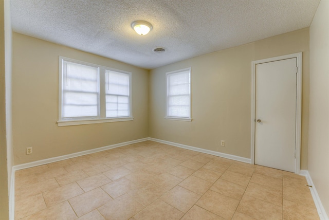 spare room with a textured ceiling, light tile patterned flooring, visible vents, and baseboards