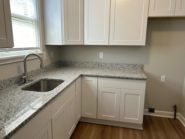 kitchen featuring white cabinets, light stone countertops, dark wood-type flooring, and a sink