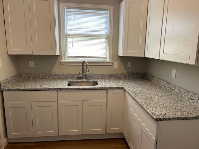 kitchen with light stone countertops, dark wood-style floors, white cabinetry, and a sink