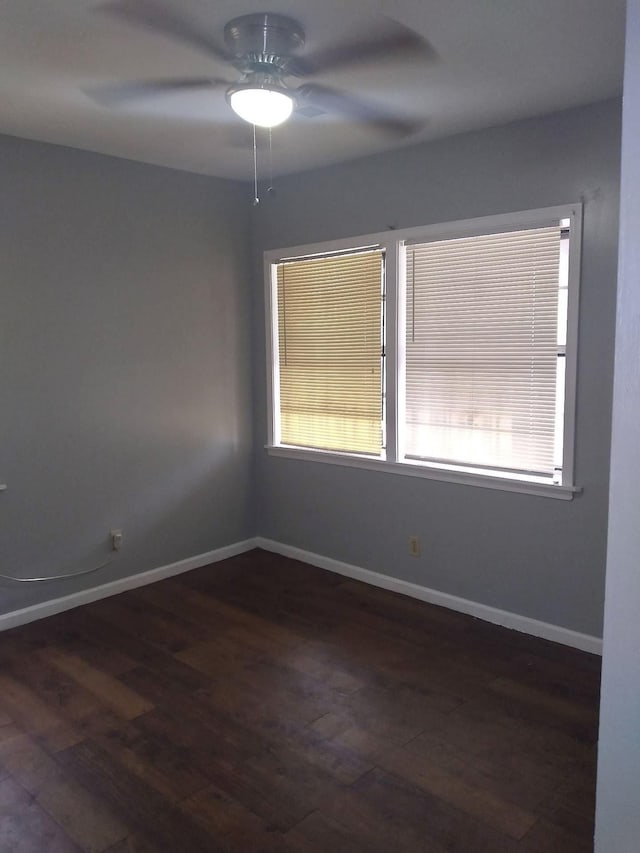 spare room featuring a ceiling fan, dark wood-style flooring, and baseboards