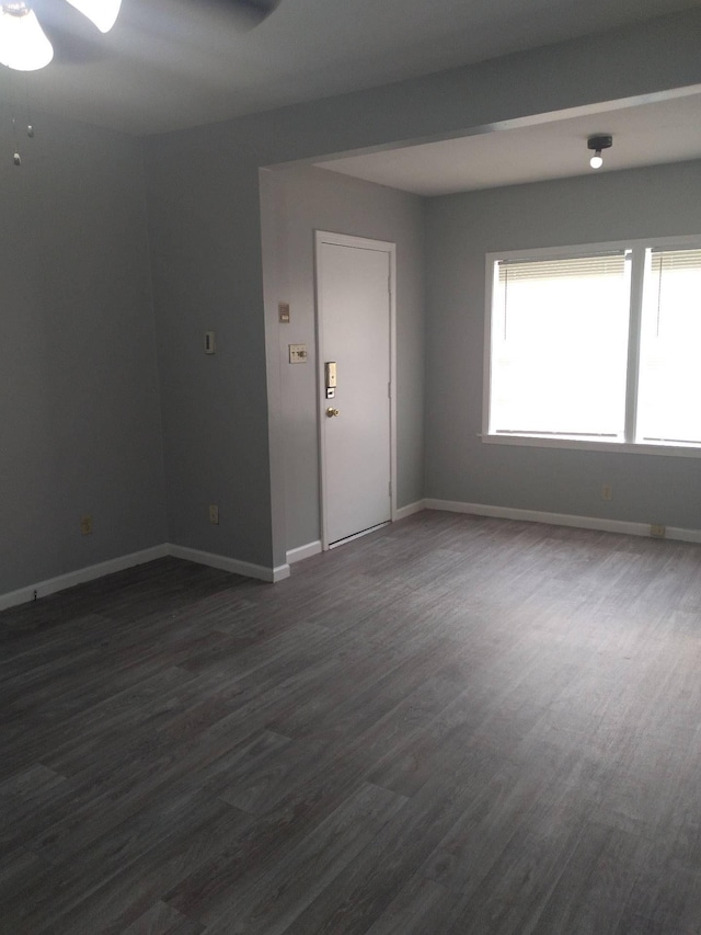 spare room featuring a ceiling fan, dark wood finished floors, and baseboards