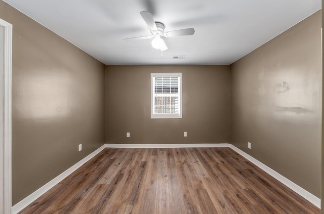 spare room featuring a ceiling fan, visible vents, baseboards, and wood finished floors