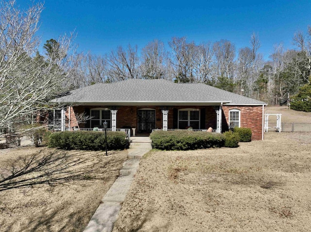 ranch-style house featuring covered porch, brick siding, a shingled roof, and fence