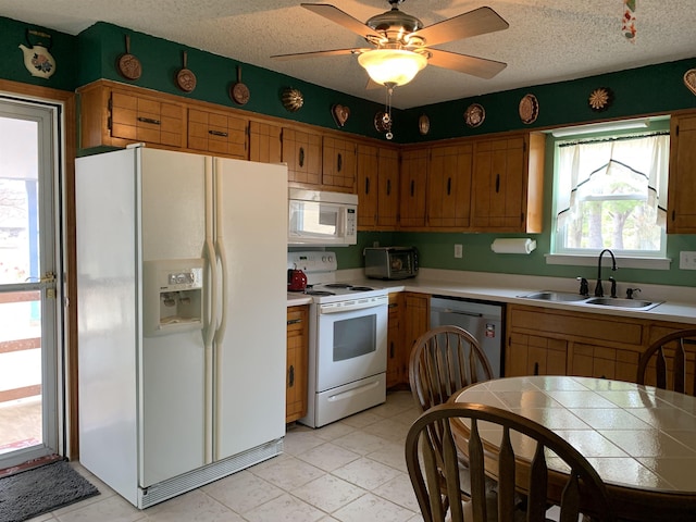 kitchen with a textured ceiling, white appliances, a sink, a ceiling fan, and brown cabinetry