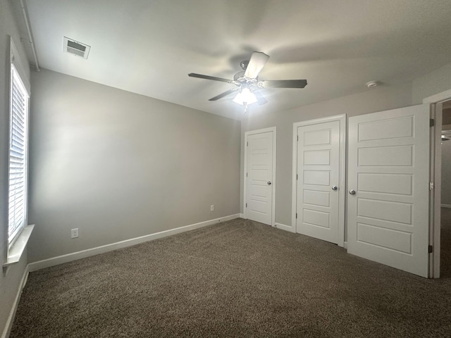 unfurnished bedroom featuring ceiling fan, baseboards, visible vents, and dark carpet