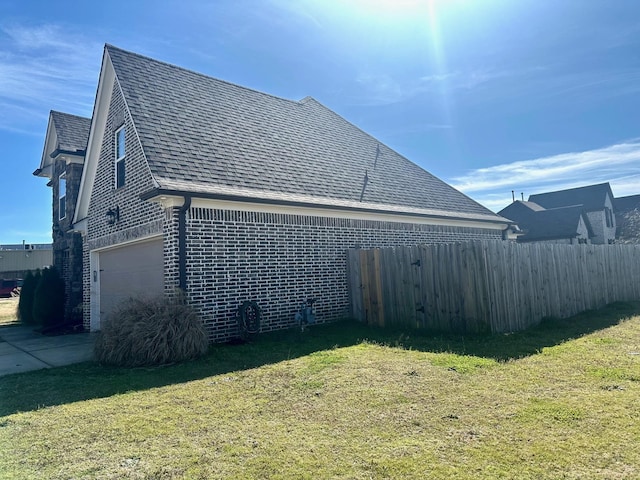 view of side of property with a garage, brick siding, a shingled roof, fence, and a lawn