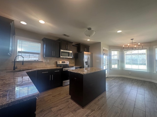 kitchen featuring stainless steel appliances, dark wood-style flooring, a sink, a center island, and decorative backsplash