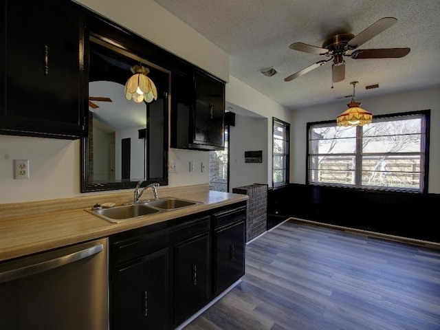 kitchen with light countertops, stainless steel dishwasher, a sink, a textured ceiling, and dark cabinetry