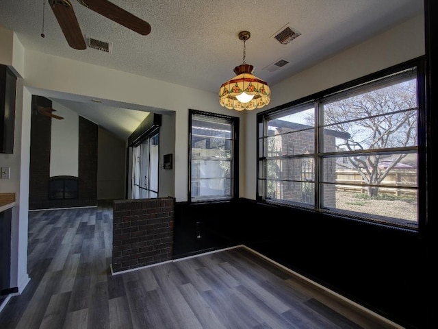 unfurnished dining area featuring a ceiling fan, a textured ceiling, visible vents, and dark wood-type flooring