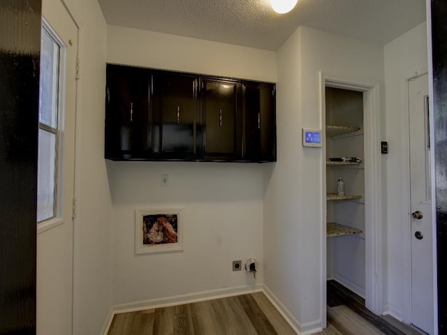 laundry room with cabinet space, electric dryer hookup, a textured ceiling, wood finished floors, and baseboards