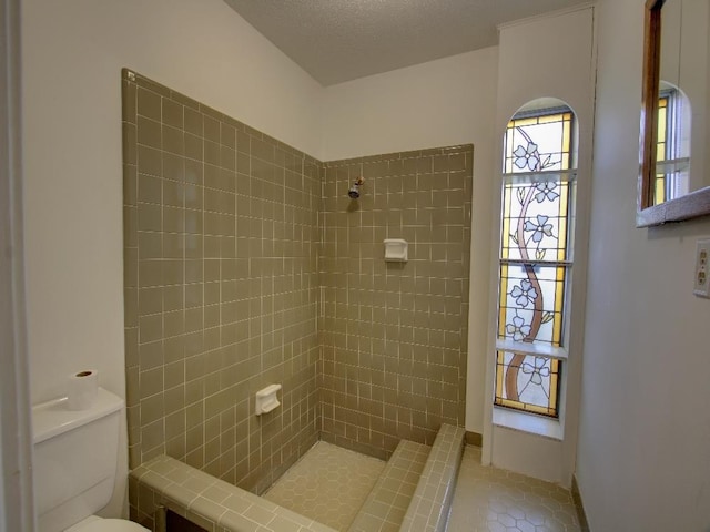 bathroom with tile patterned flooring, tiled shower, a textured ceiling, and toilet