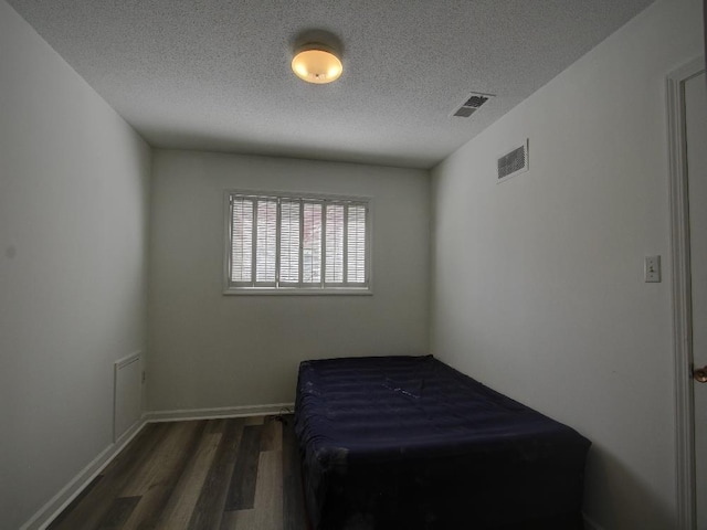 bedroom featuring a textured ceiling, wood finished floors, visible vents, and baseboards