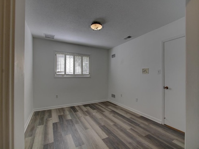 spare room with a textured ceiling, wood finished floors, visible vents, and baseboards