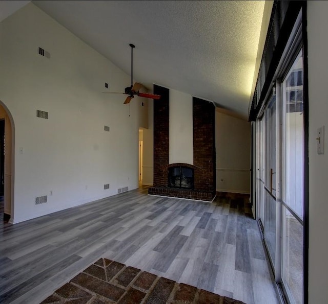 unfurnished living room with arched walkways, visible vents, a brick fireplace, a textured ceiling, and wood finished floors