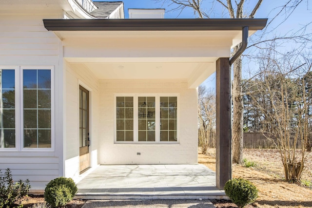 view of exterior entry featuring a patio area, fence, and roof with shingles