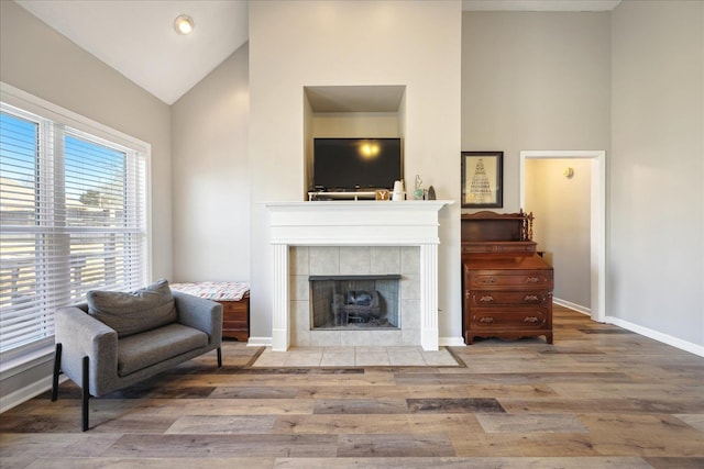 sitting room featuring high vaulted ceiling, a tile fireplace, wood finished floors, and baseboards