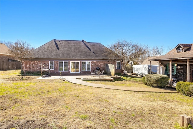 rear view of house featuring a patio, a shingled roof, brick siding, fence, and a yard