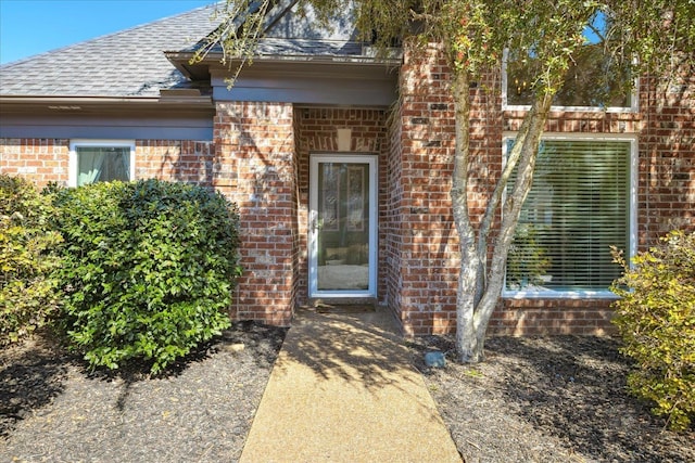 entrance to property featuring a shingled roof and brick siding