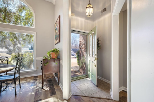 entrance foyer with wood finished floors, a towering ceiling, baseboards, visible vents, and an inviting chandelier