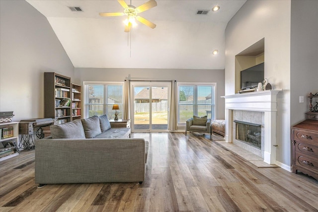 living area featuring high vaulted ceiling, a fireplace, visible vents, and wood finished floors