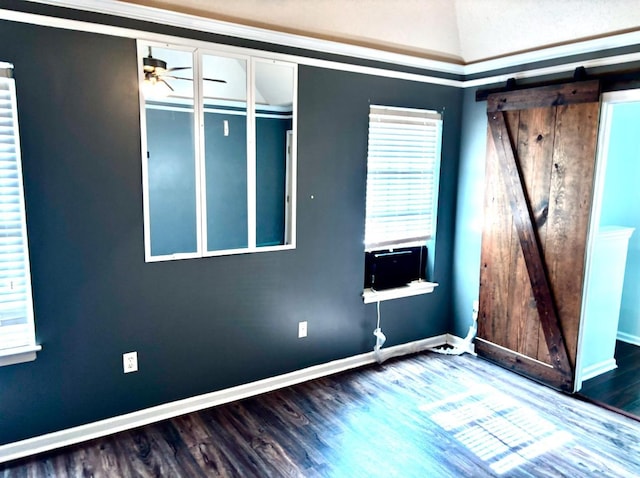 unfurnished room with ceiling fan, a barn door, wood finished floors, and baseboards