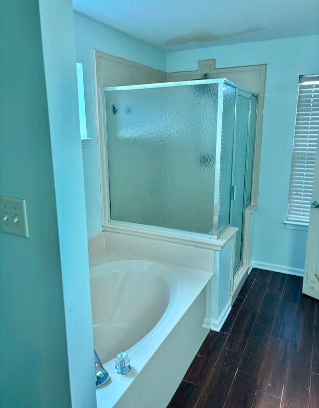 bathroom with a garden tub, a shower stall, baseboards, and wood finished floors