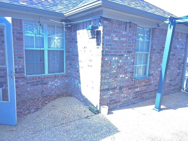 entrance to property with roof with shingles and brick siding