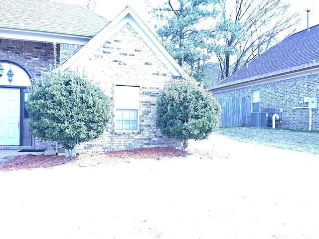 view of home's exterior featuring a shingled roof, central AC, and brick siding