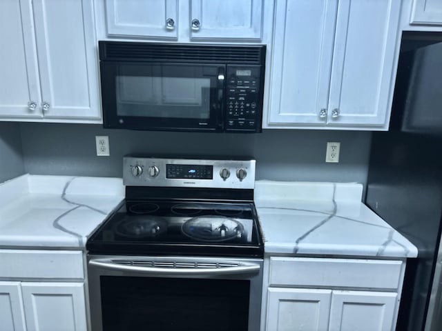 kitchen with light stone countertops, black microwave, white cabinets, and stainless steel electric stove