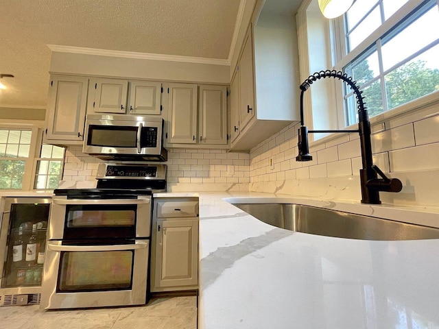 kitchen with light stone counters, wine cooler, appliances with stainless steel finishes, ornamental molding, and a sink