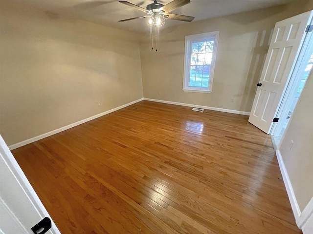 spare room featuring a ceiling fan, visible vents, baseboards, and wood finished floors