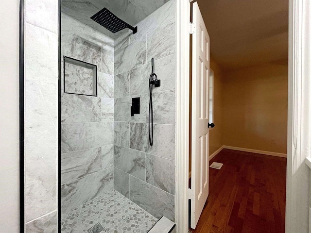 full bathroom with wood finished floors, a tile shower, and baseboards