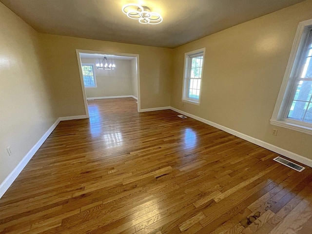 unfurnished room with a chandelier, visible vents, baseboards, and wood finished floors