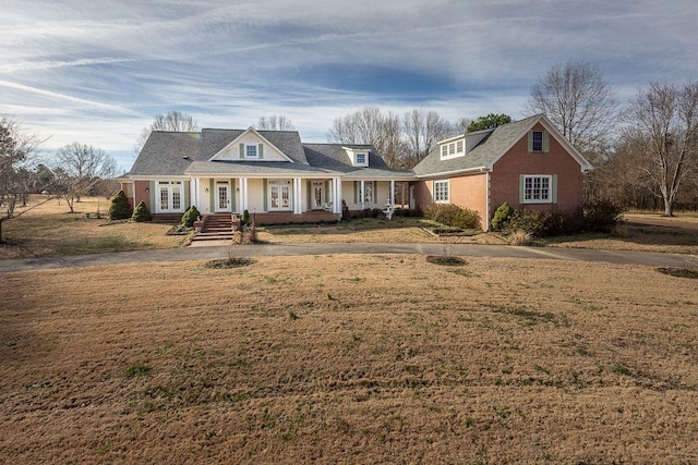 view of front of home featuring french doors, covered porch, brick siding, and a front lawn