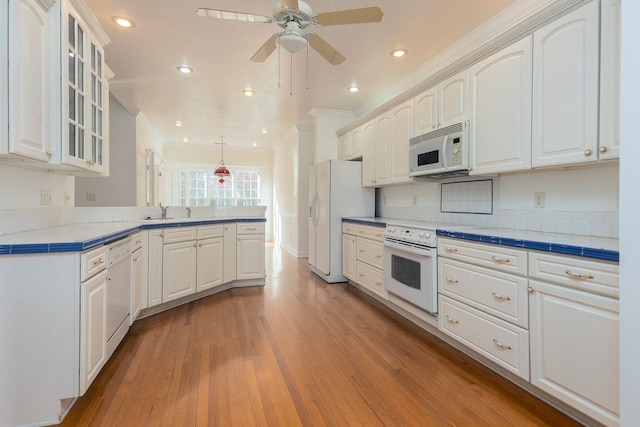 kitchen with white appliances, glass insert cabinets, wood finished floors, a peninsula, and white cabinetry