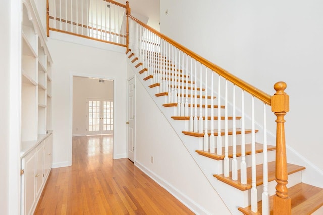 stairs featuring french doors, a high ceiling, wood finished floors, and baseboards