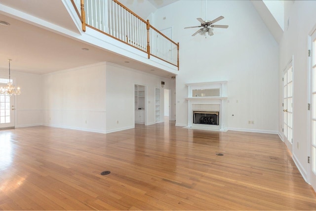 unfurnished living room featuring light wood finished floors, a towering ceiling, a fireplace with flush hearth, baseboards, and ceiling fan with notable chandelier