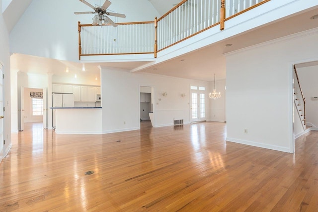 unfurnished living room with ceiling fan with notable chandelier, a high ceiling, baseboards, light wood-style floors, and crown molding