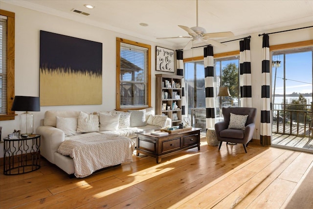 living area with a ceiling fan, visible vents, ornamental molding, and hardwood / wood-style floors