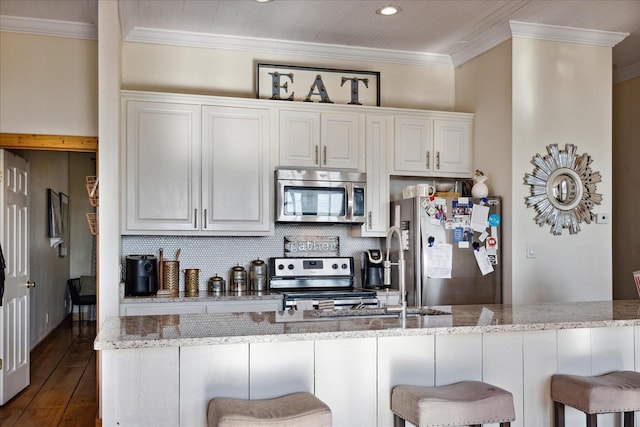 kitchen featuring appliances with stainless steel finishes, crown molding, decorative backsplash, and a breakfast bar area