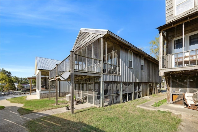 rear view of house with metal roof, a yard, and a sunroom