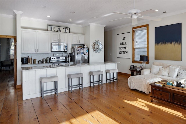 kitchen with hardwood / wood-style flooring, stainless steel appliances, white cabinets, ornamental molding, and a kitchen bar