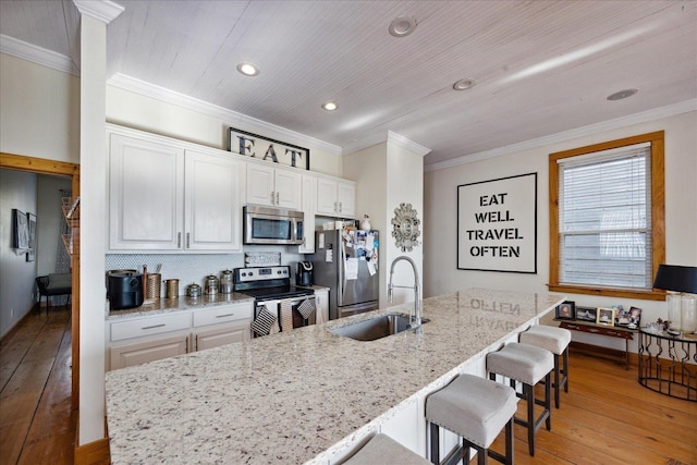 kitchen with appliances with stainless steel finishes, a kitchen breakfast bar, ornamental molding, light wood-type flooring, and a sink