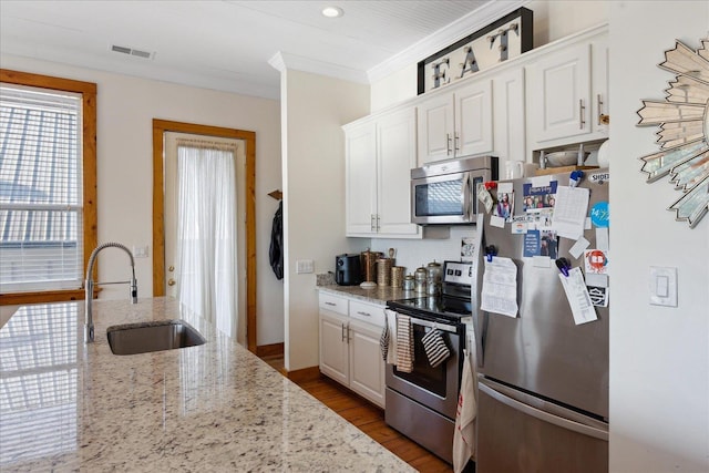 kitchen with wood finished floors, a sink, white cabinetry, appliances with stainless steel finishes, and crown molding