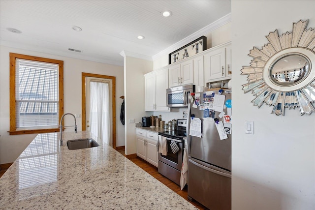 kitchen with light stone counters, appliances with stainless steel finishes, ornamental molding, white cabinets, and a sink