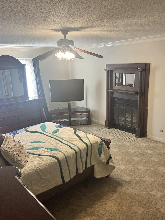 carpeted bedroom featuring baseboards, a glass covered fireplace, ceiling fan, a textured ceiling, and crown molding