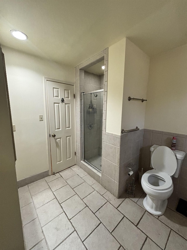 bathroom with a wainscoted wall, a shower stall, toilet, and tile walls