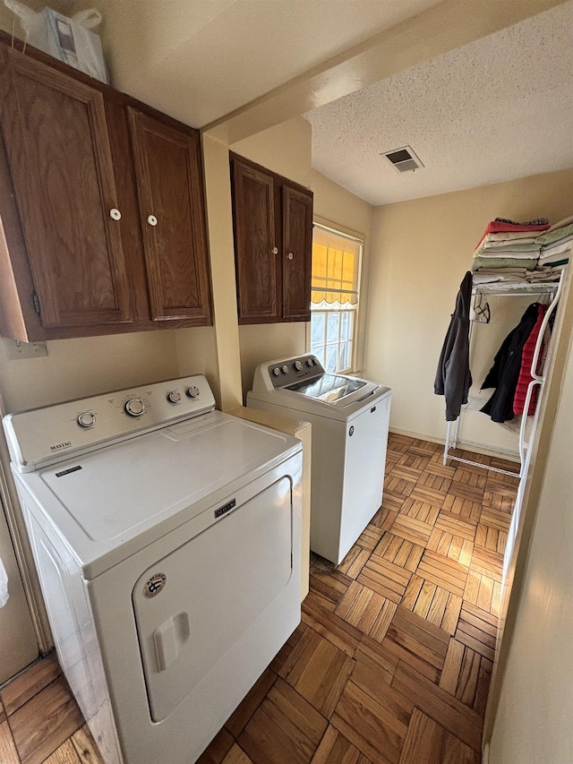 clothes washing area featuring a textured ceiling, visible vents, washer and clothes dryer, and cabinet space