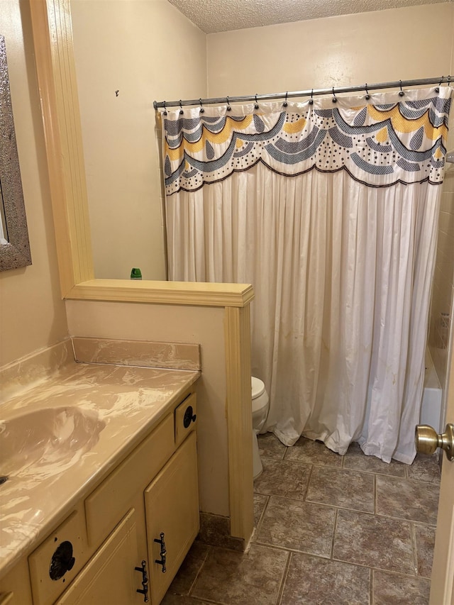 full bath featuring toilet, stone finish floor, a textured ceiling, and vanity